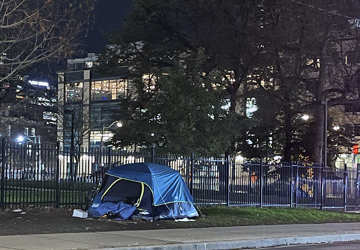 A photo of a blue tent set up on a city sidewalk with the well-lit housing behind it.