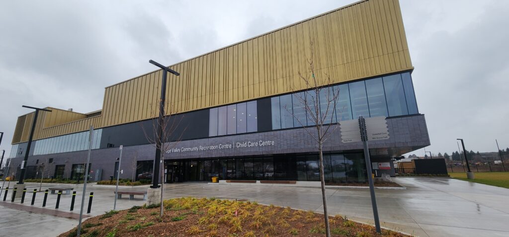 Exterior view of the Rouge Valley Community Recreation Centre showing its large gold-coloured upper façade, glass windows and entrance area on a cloudy day.