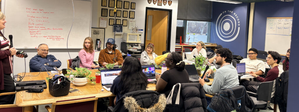 A photo of students gathered around a wooden table in the OTR newsroom.