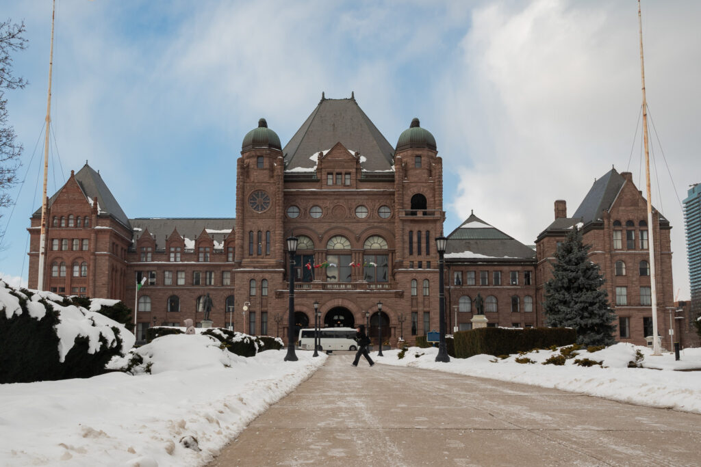 The front of Ontario's legislature Queen's Park seen from near ground, with snow lining and blue cloudy sky.