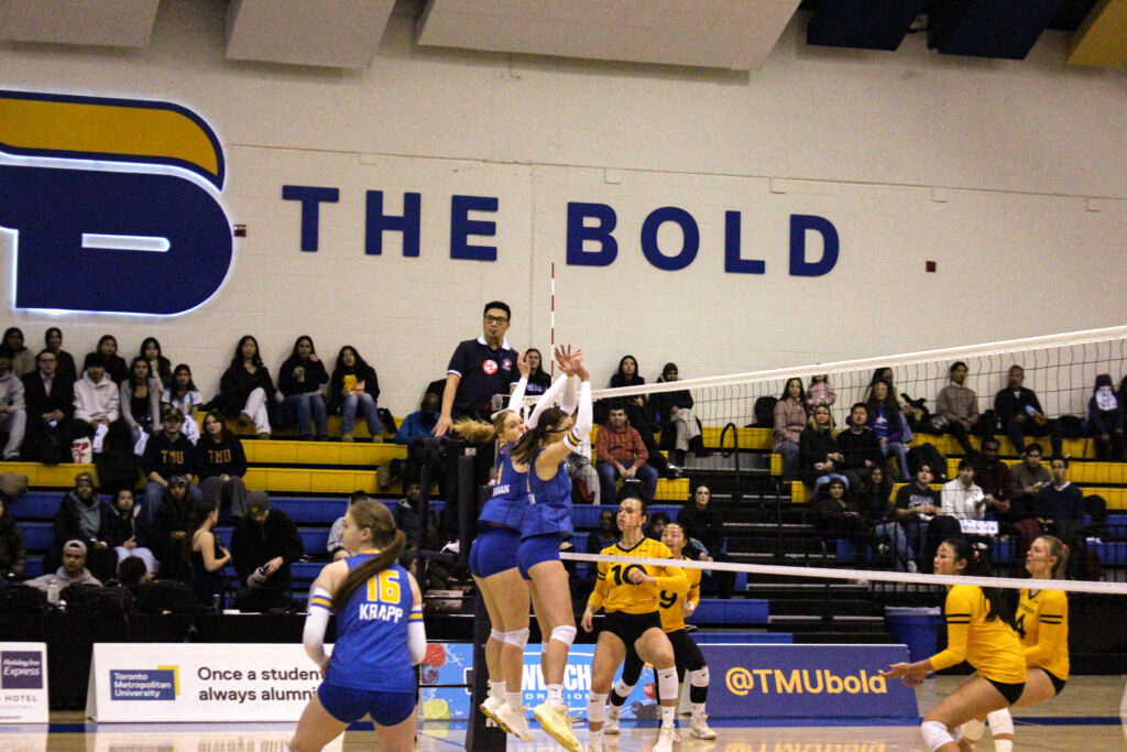Two women's volleyball players jump at the same time during a game.