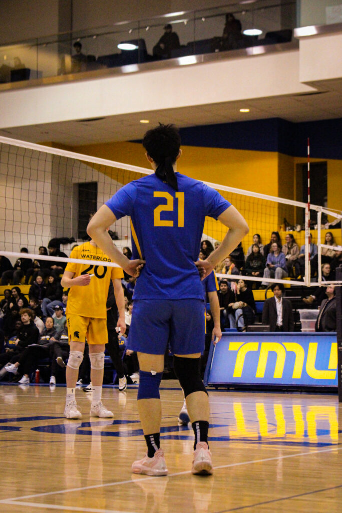 A men's volleyball player stands on the court during a game.