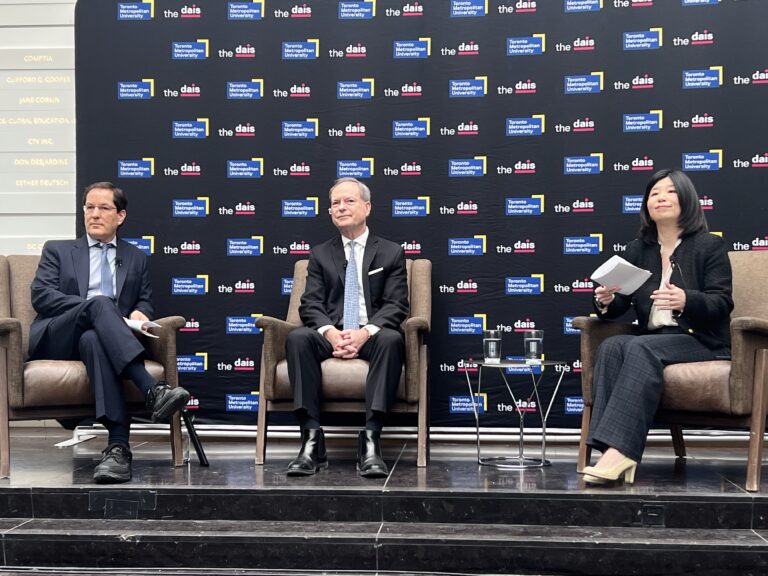 Ontario Finance Minister Peter Bethlenfalvy sits on stage with two other panelists at Toronto Metropolitan University. They are engaged in a discussion about the upcoming 2026 provincial budget, with microphones in hand and an audience watching the forum.