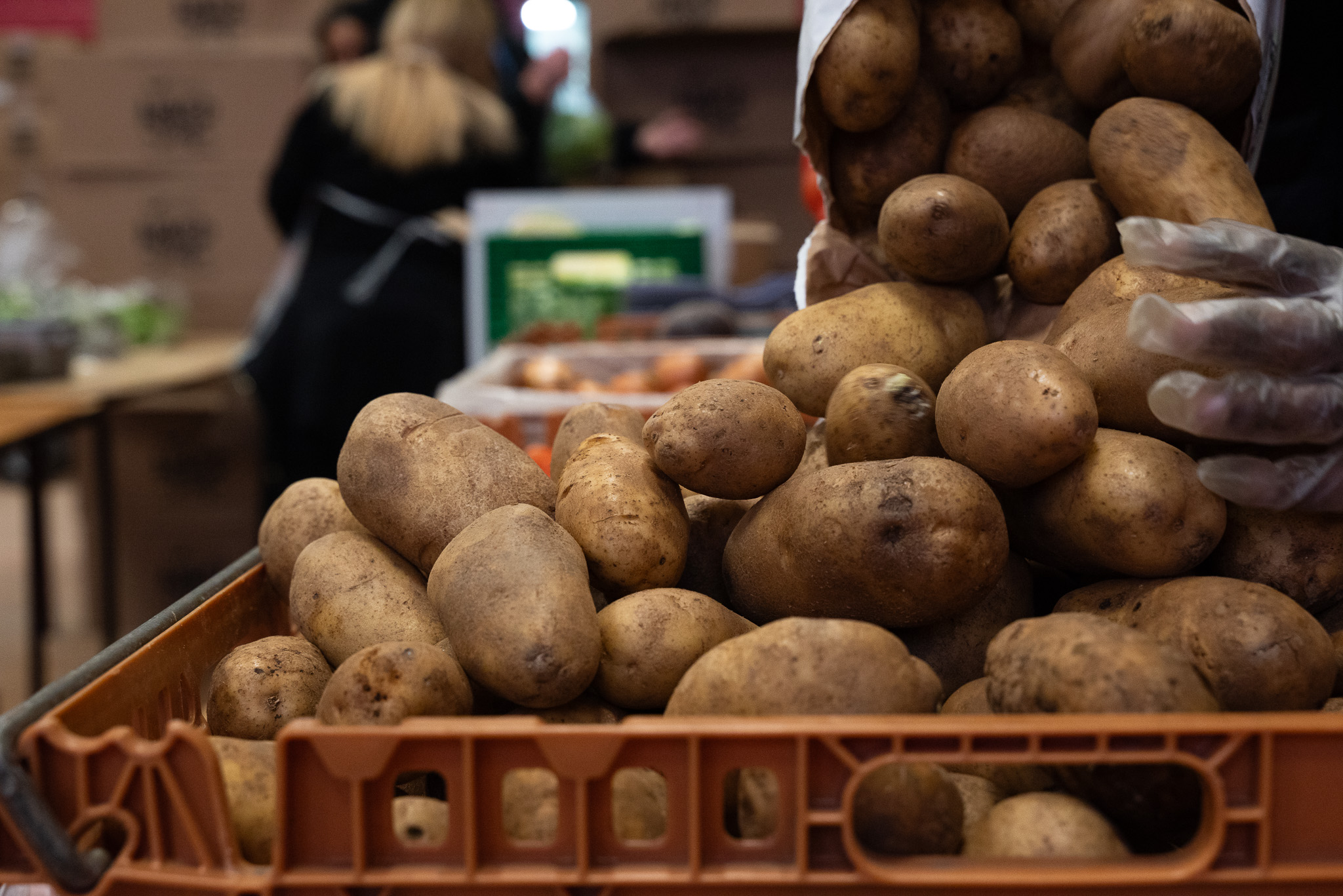Potatoes fall out of a bag into a basket, pushed on by a hand with a glove.