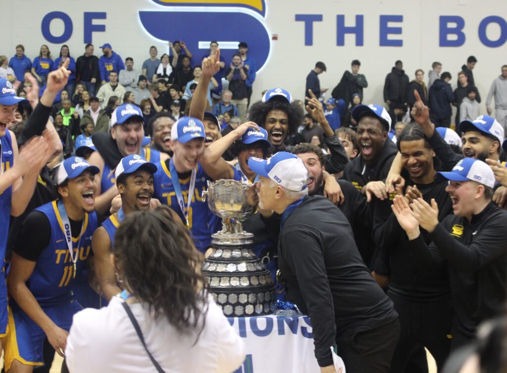 A coach kisses a trophy in front of a basketball team.
