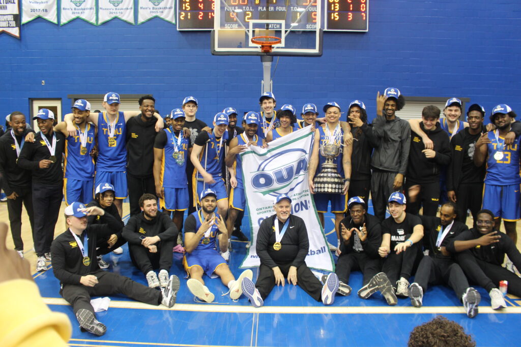 A basketball team poses with a trophy and a banner. 