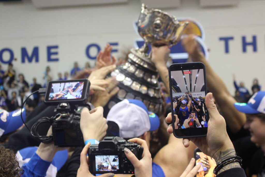 A number of cameras trying to capture a team lifting a trophy.