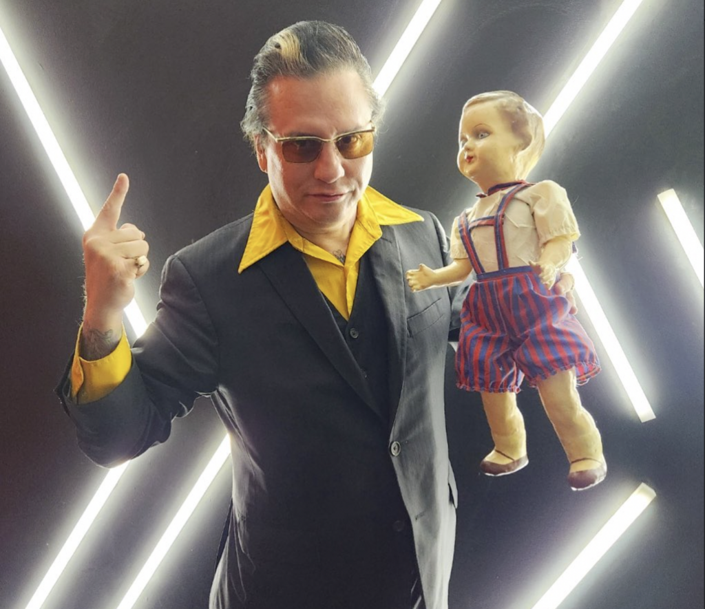 Mysterion the Mindreader and his haunted companion Man wearing a suit and sunglasses holding a doll