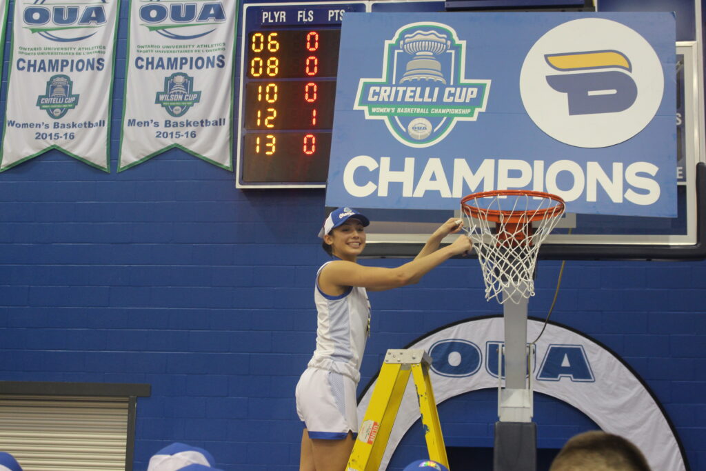 A basketball player cuts the net of a basket after winning a game. 