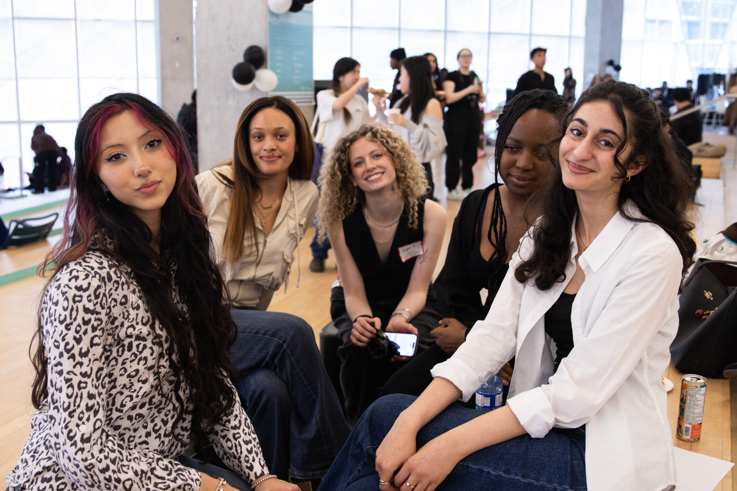 Five women pose sitting down in front of a camera.