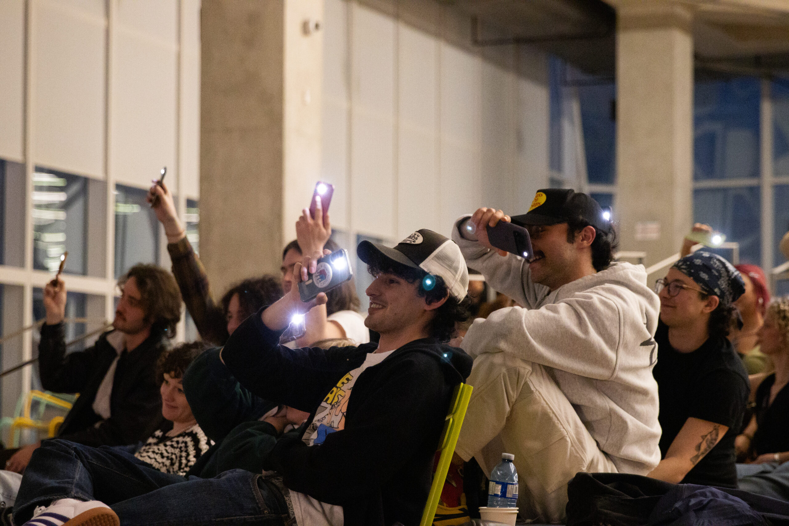 A group of people watching something holds up their phone flashlights.