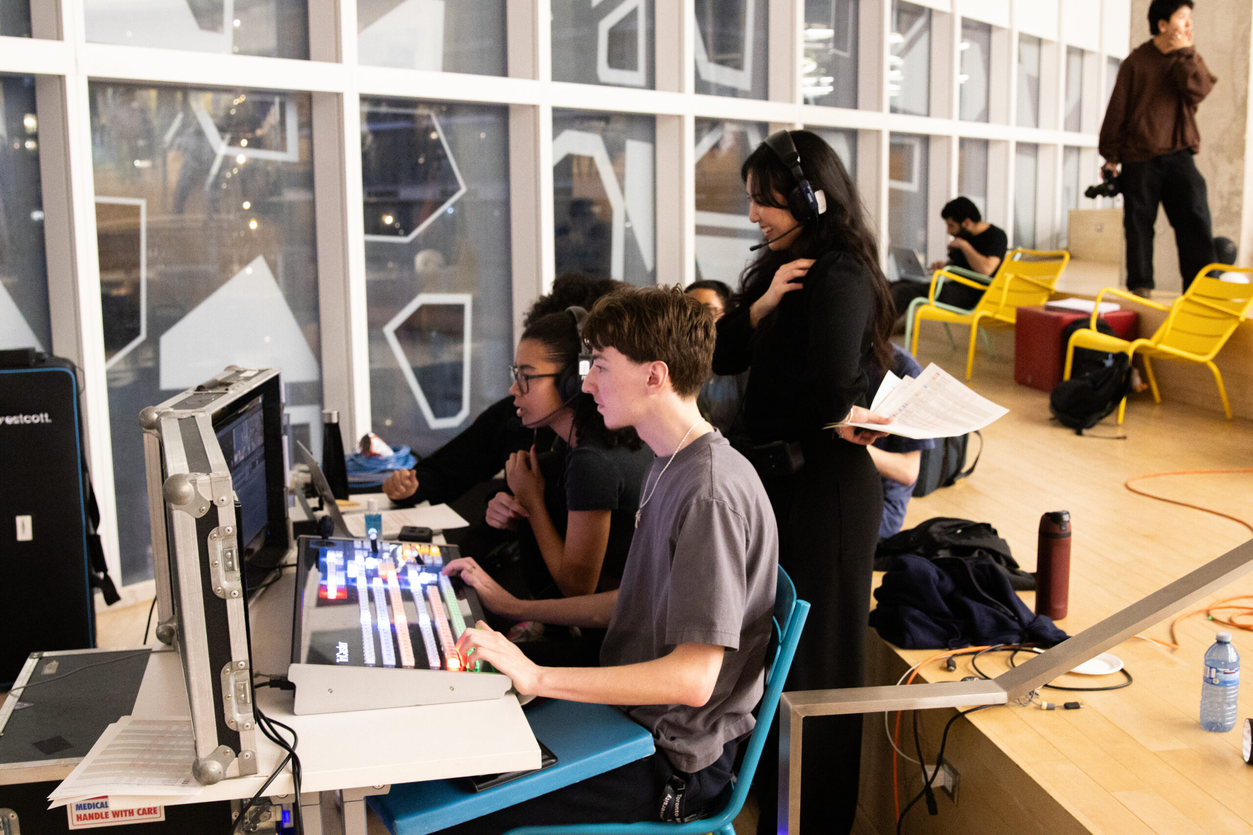Three students sitting behind a lighting and sound panel.