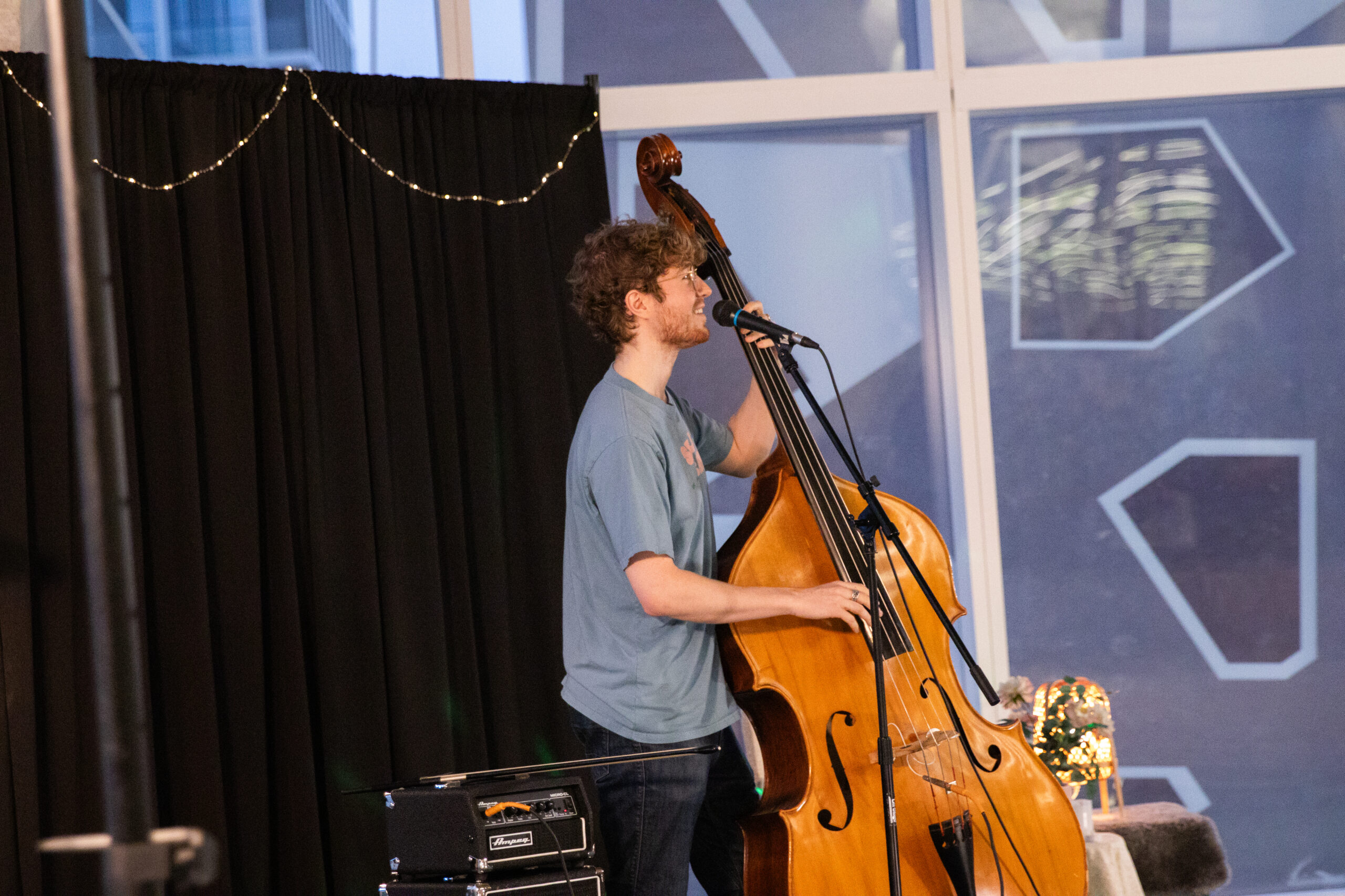 Man plays double bass in front of a microphone to an audience.
