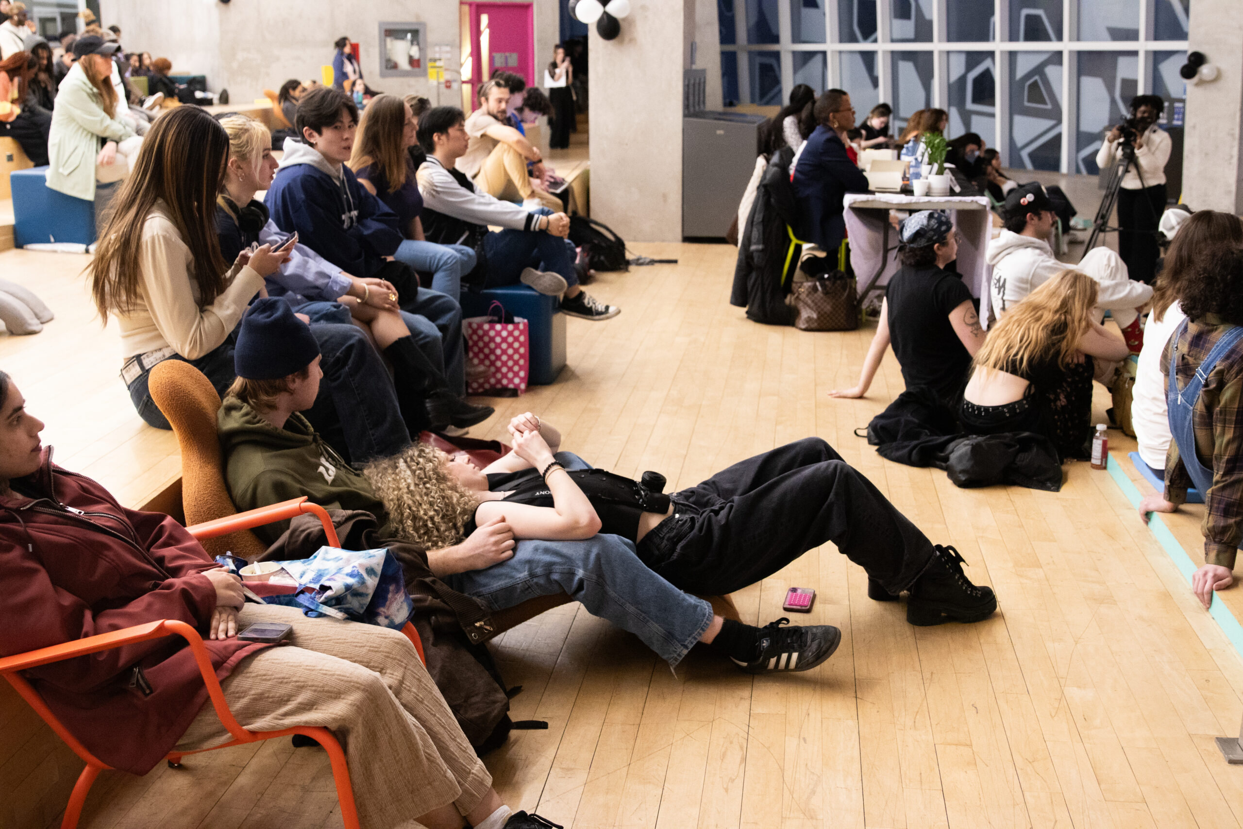Students sitting on the floor watching something in front of them.