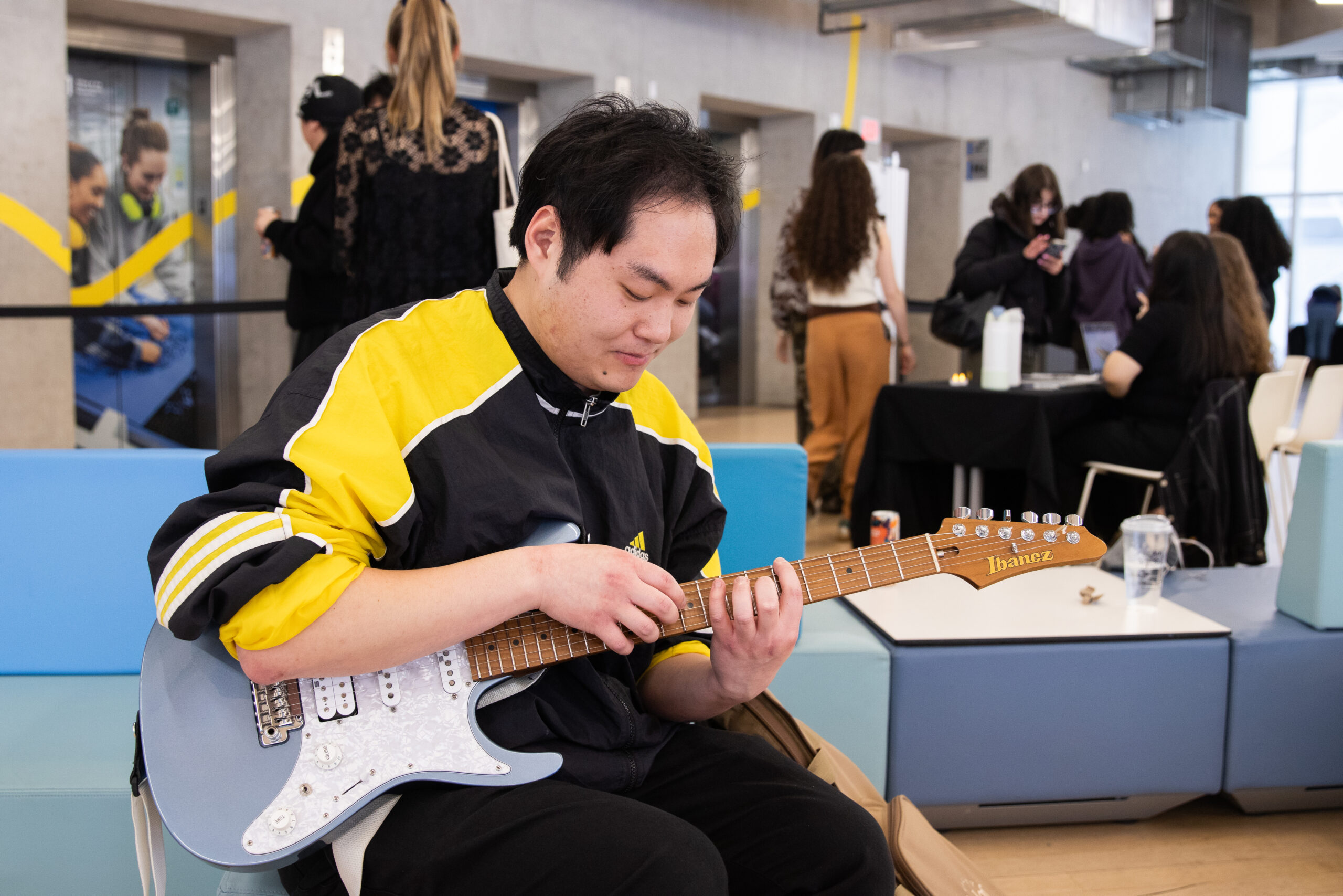 Man holds electric guitar while sitting on a couch and playing.