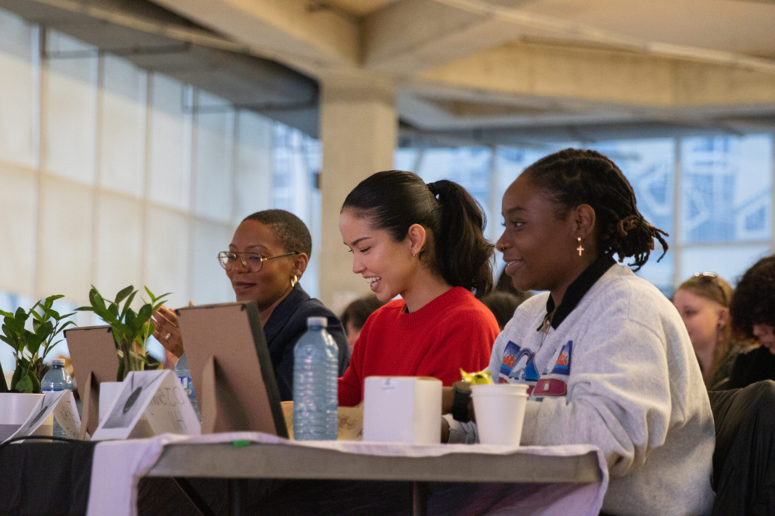 Three women sit in front of a table watching something.