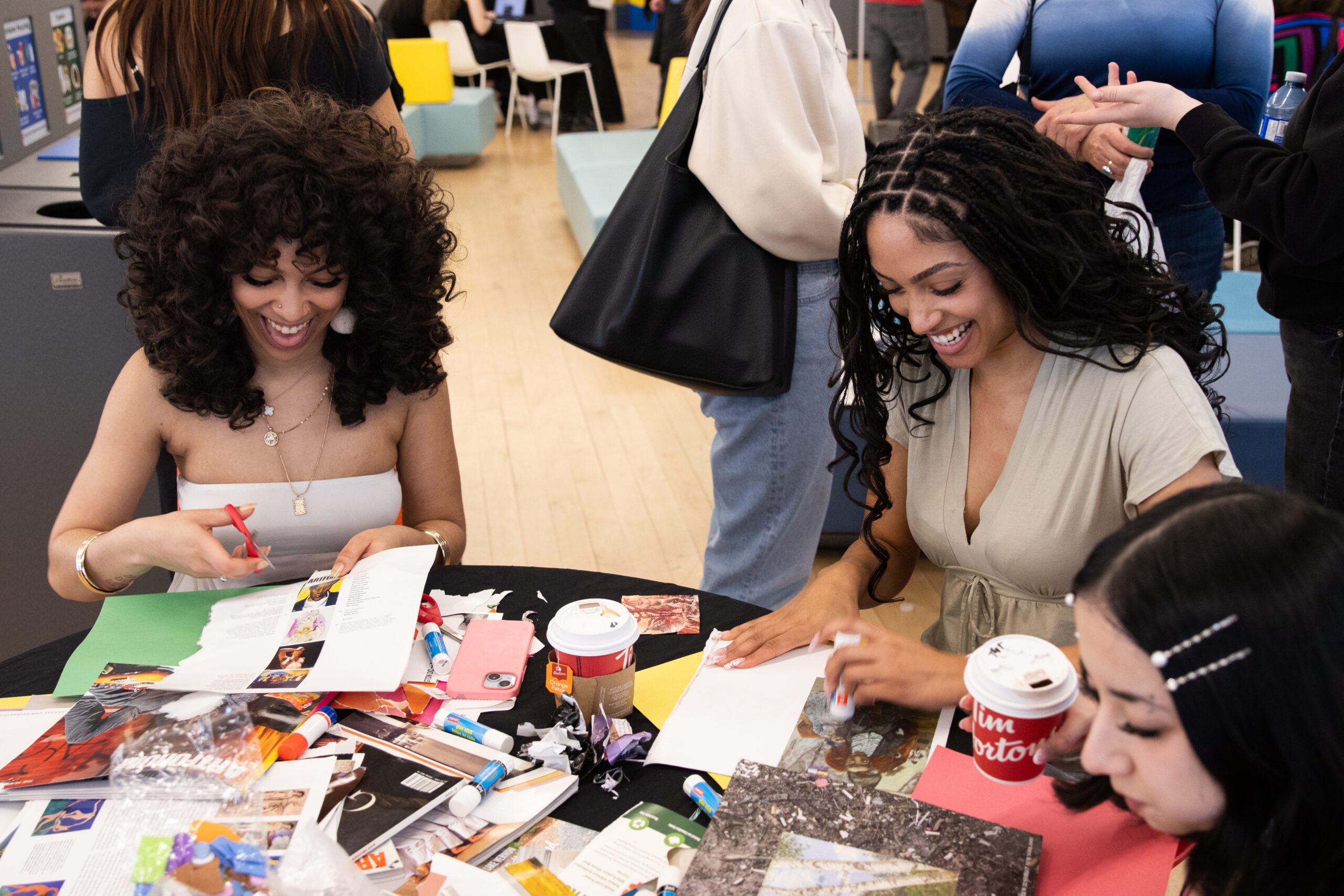 Two women sit at a table and craft with others.