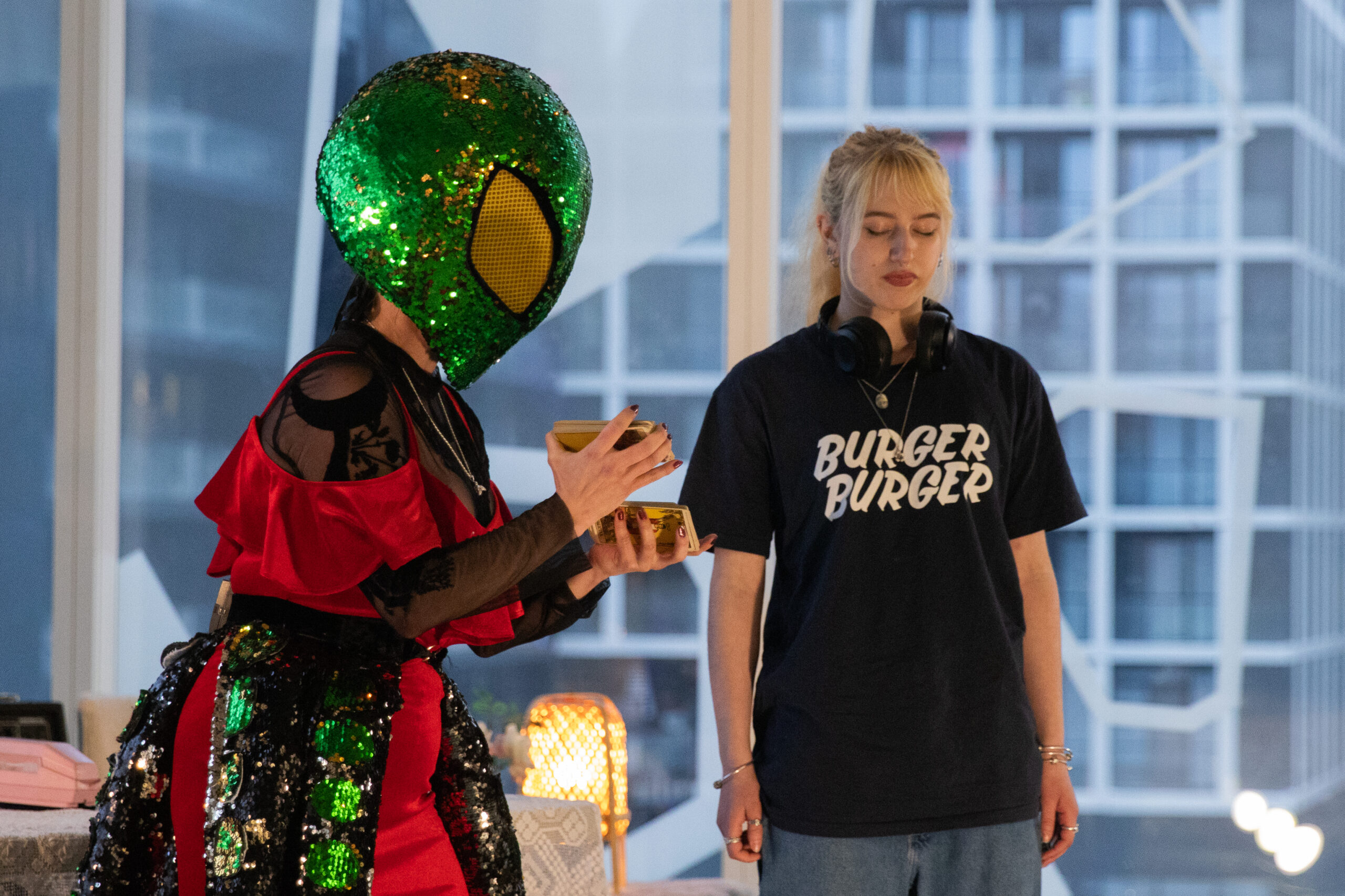 Person dressed in alien costume reading tarot cards to an audience member.