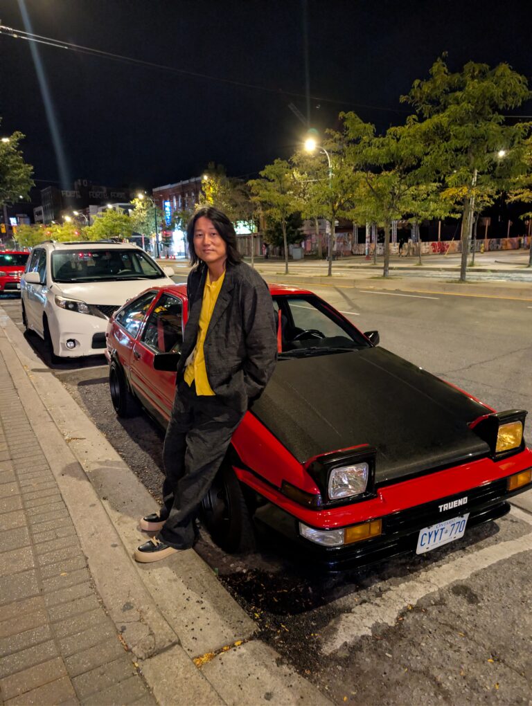 Image of actor Sung Kang leaning against a red car.
