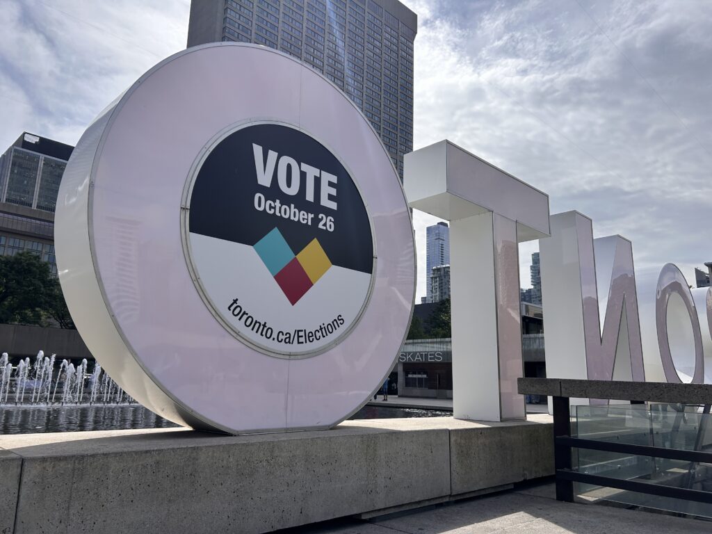 The back of the Toronto sign outside of Toronto City Hall. On the Back of one "O" is a sign saying "Vote October 26." and toronto.ca/Elections