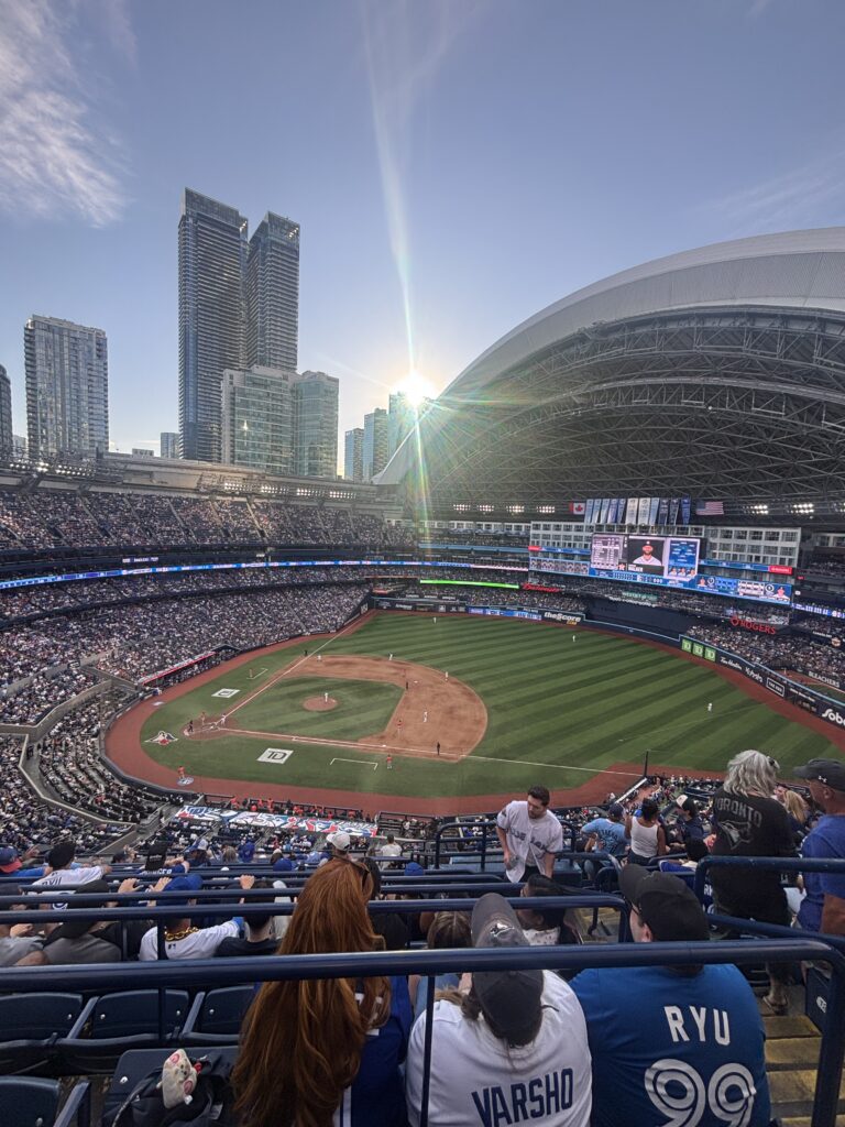 Picture of a sun setting at Rogers Centre, the dome open and the stadium filled with players and fans. 