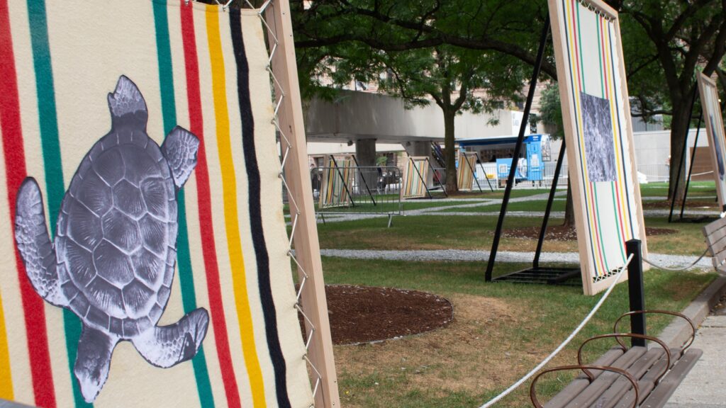 Blankets with printed images being held by wooded canvas outside surrounded by trees.