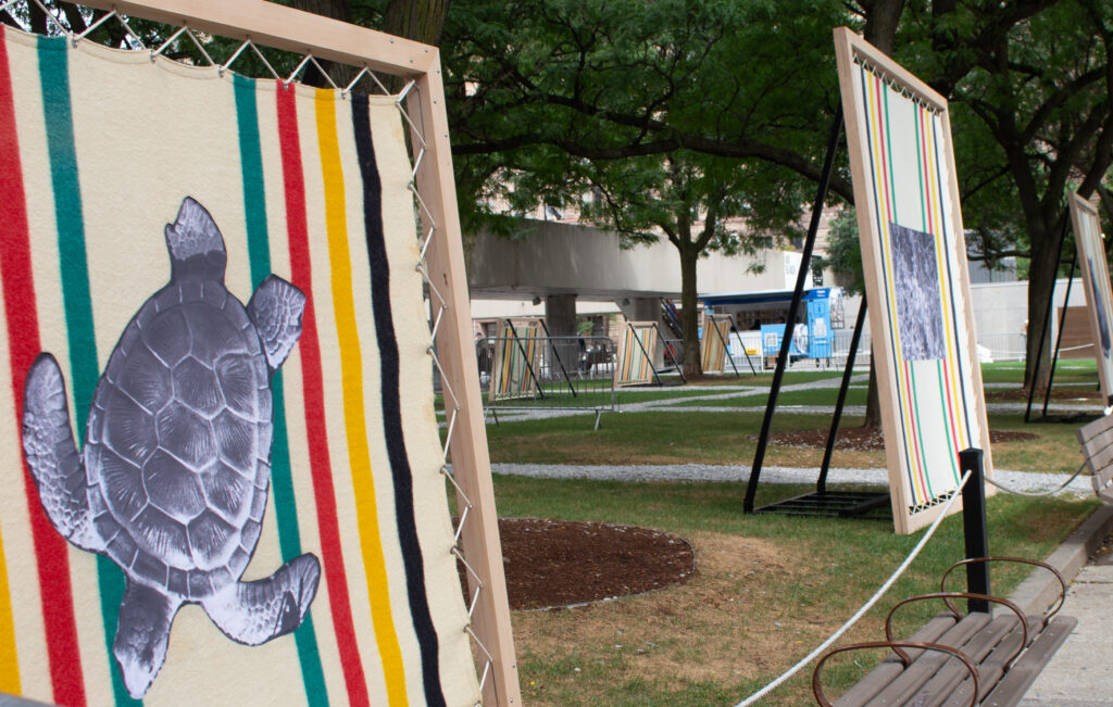 Blankets with printed images being held by wooded canvas outside surrounded by trees.