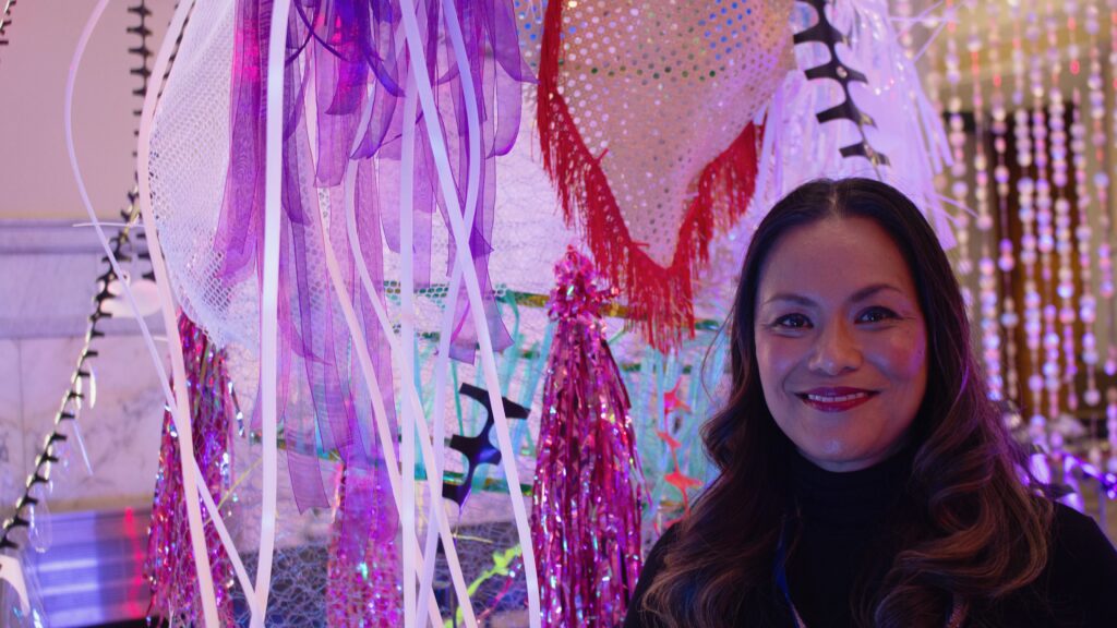 A female standing beside streamers and being shined by purple lighting.