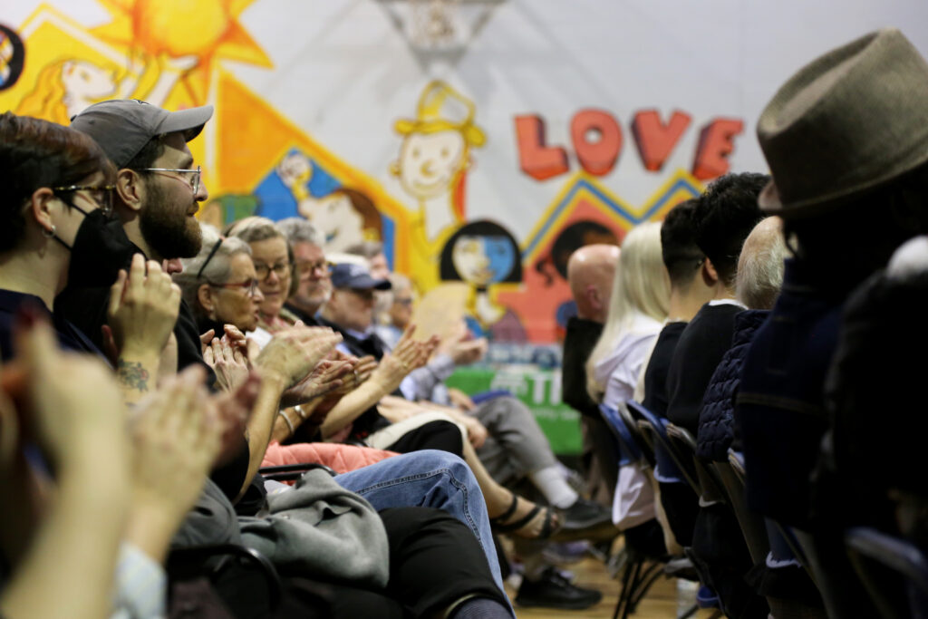A row of people clapping while sitting in a row of chairs facing forward.