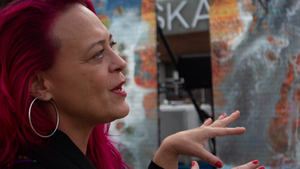 A woman with pink hair looking at digital panels.