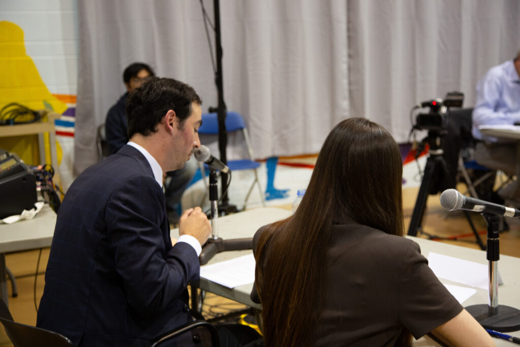 Two people sitting behind a desk with mics in front of them.