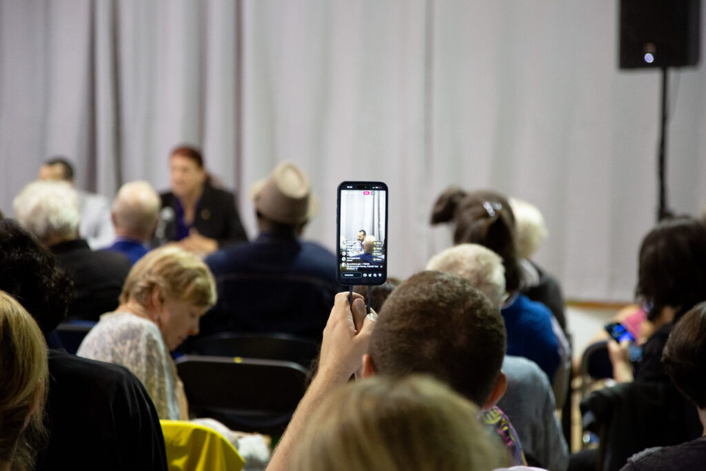 An audience member holds up a smartphone showing a livestream of the Toronto municipal election debate.