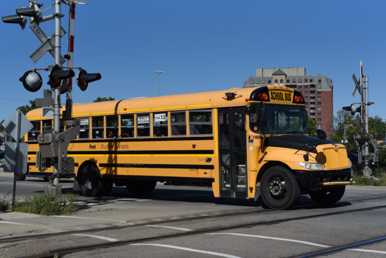 Yellow school bus at a railway crossing with raised barriers.