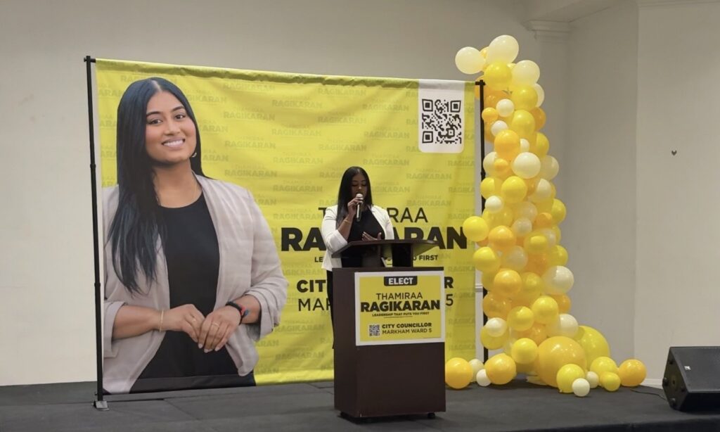 A young woman speaking at a podium with a campaign sign for "Thamiraa Ragikaran, City Councillor Markham Ward 5."