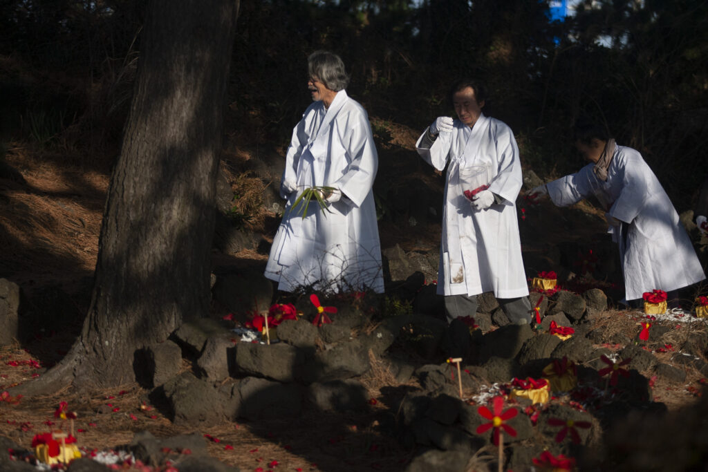 Three men dressed in burial shrouds are undergoing funeral rites.